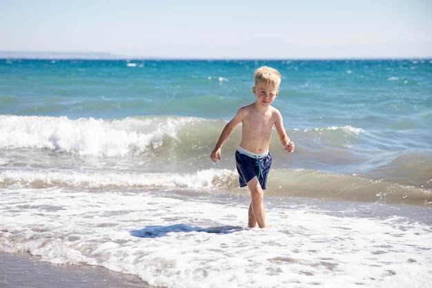 Netter kleiner Junge, der am Strand am Meer spielt, ist er glücklich Konzept Sommerferien Restspaß