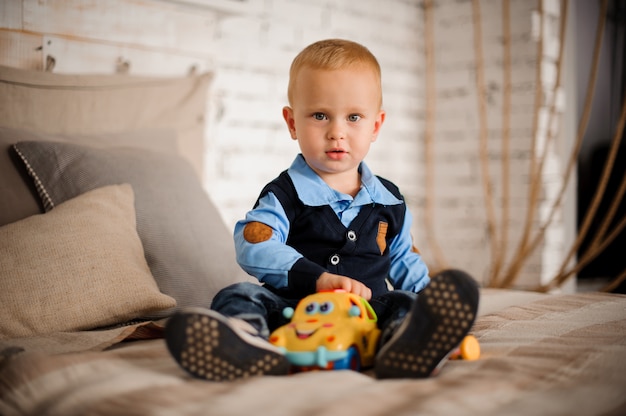 Netter kleiner Junge, der auf dem Bett mit einem Spielzeug sitzt