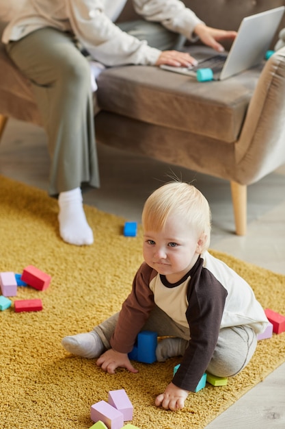 Netter kleiner Junge, der auf dem Boden sitzt und mit bunten Blöcken im Raum spielt