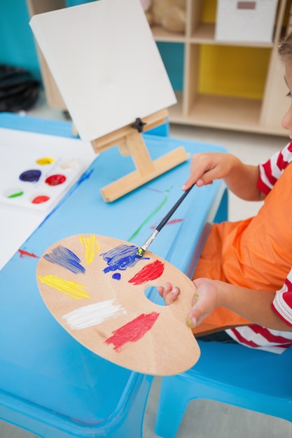 Netter kleiner Junge, der bei Tisch im Klassenzimmer malt