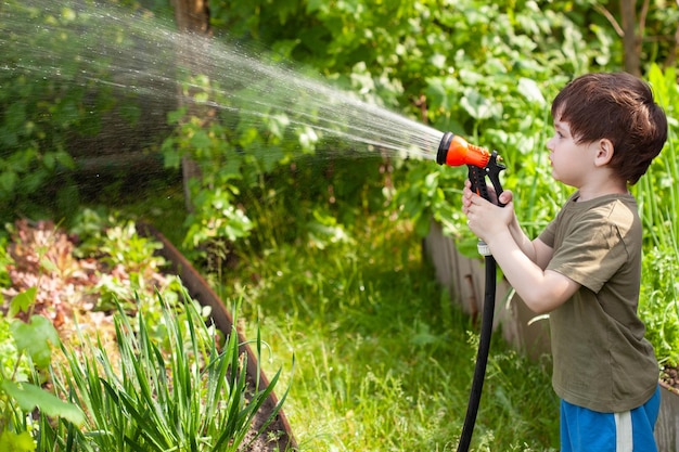 Netter kleiner Junge, der Blumen im Garten am Sommertag gießt Lustiges Kind, das Pflanzen im Hof gießt