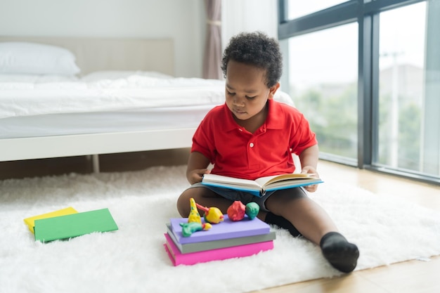 Netter kleiner Junge, der ein Buch auf einem weißen Boden im Schlafzimmer liest