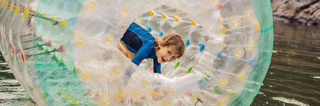 Netter kleiner Junge, der im Zorb einen rollenden Plastikzylinderring mit einem Loch in der Mitte auf dem spielt