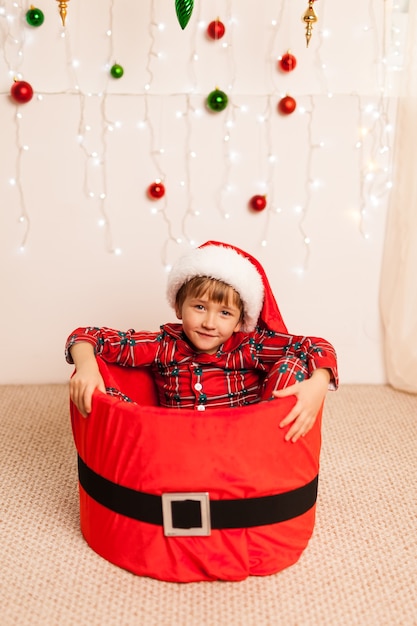 Netter kleiner Junge, der in einem roten Korb mit Weihnachtsmannmütze sitzt