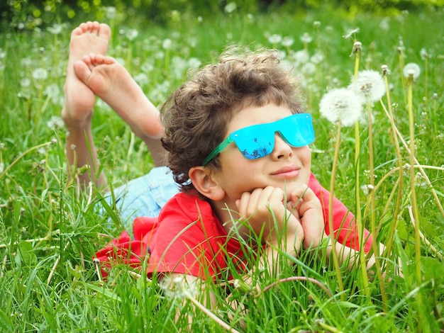 Netter kleiner Junge, der mit Löwenzahn auf dem Gras liegt