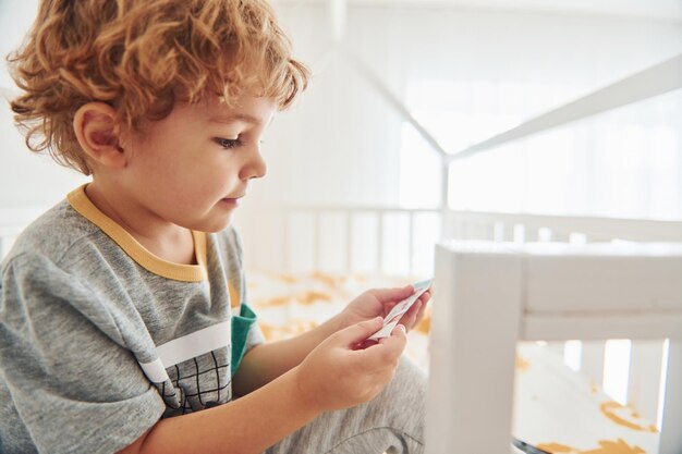 Netter kleiner Junge, der sich ausruht und drinnen im Schlafzimmer Spaß hat