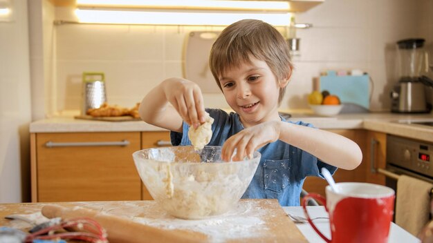 Foto netter kleiner junge, der teig knetet und zutaten in einer großen glasschüssel mischt