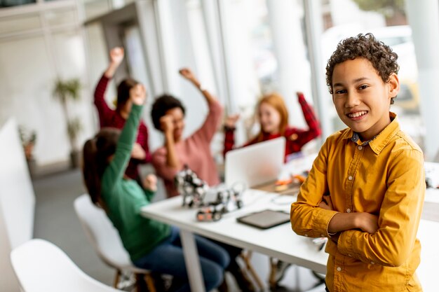 Netter kleiner Junge, der vor Gruppe von Kindern steht, die elektrisches Spielzeug und Roboter am Robotikklassenzimmer programmieren