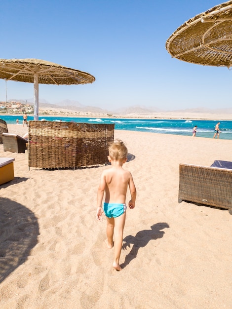 Netter kleiner Junge, der zum Meer geht und Meereswellen betrachtet. Kinder entspannen und haben eine gute Zeit während der Sommerferien.