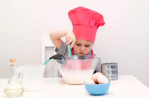 Netter kleiner Junge in einer roten Kochmütze knetet den Gebäckteig in einer Schüssel. Hausgemachte Kuchen.