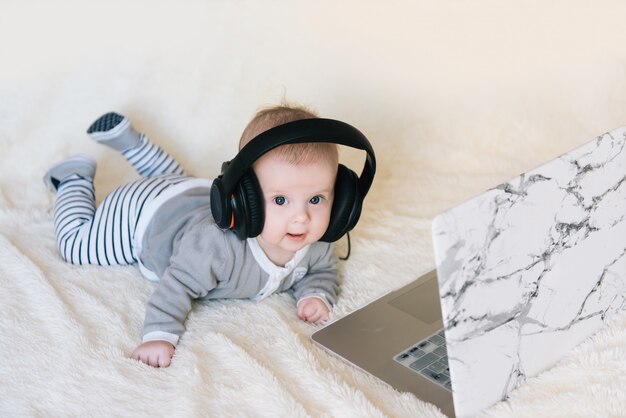 Netter kleiner Junge liegt in Kopfhörern und schaut in Laptop