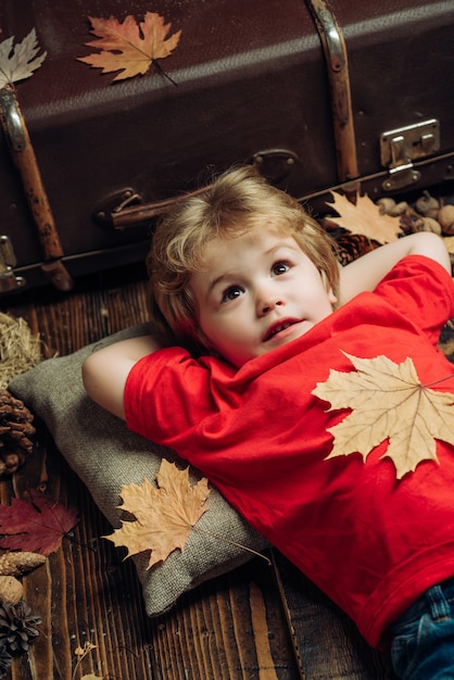 Netter kleiner Junge macht sich bereit für den Herbst. Blonder kleiner Junge, der mit Blatt auf Bauchlügen ruht