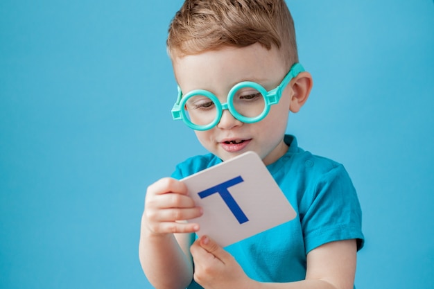 Netter kleiner Junge mit Brief auf Hintergrund. Kind lernt Briefe. Alphabet.