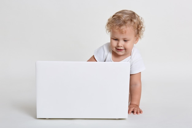 Netter kleiner Junge mit weißem Laptop, der Bildschirm mit Interesse betrachtet