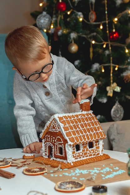 Netter kleiner Junge schmückt Weihnachtslebkuchenhaus