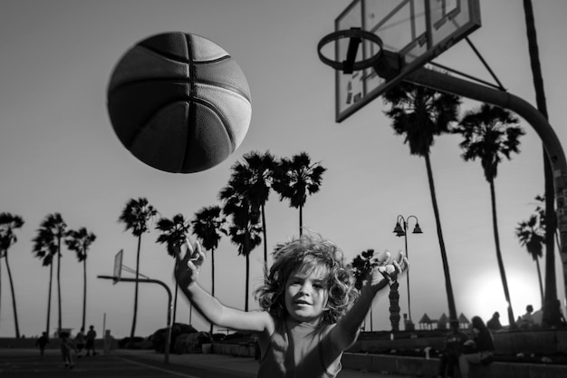 Netter kleiner Junge spielt Basketball aktive Kinder, die ein Spiel im Freien mit Basketballball auf Venice Bea genießen