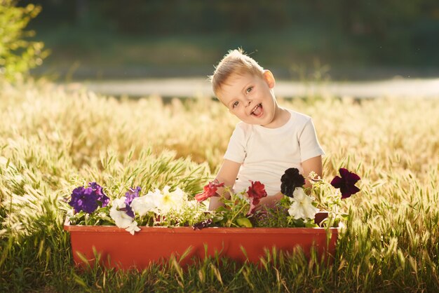 Netter kleiner Kinderjunge, der Blumensämlinge in einem Topf im Garten auf Sonnenuntergang wässert. Lustiger kleiner Gärtner. Frühlingskonzept, Natur und Pflege.