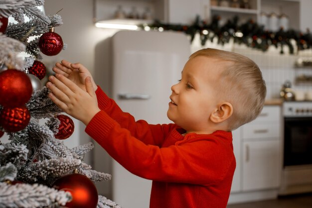 Netter kleiner Kinderjunge, der zu Hause Weihnachtsbaum verziert