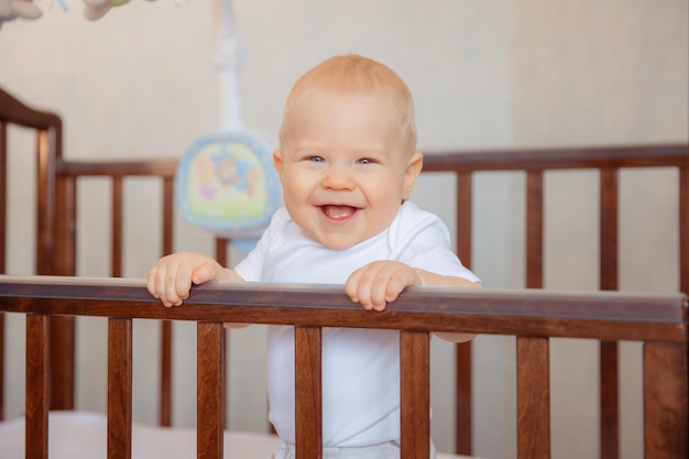Netter kleiner neugeborener Junge sitzt in einer Krippe Babyjunge sitzt lächelnd in der Krippe