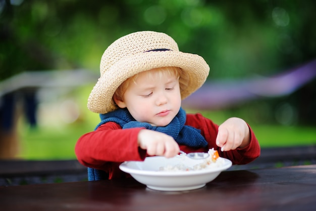 Netter Kleinkindjunge, der draußen Reisgetreide isst. Gesundes Essen für kleine Kinder