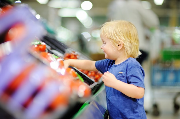 Netter Kleinkindjunge in einem Lebensmittelgeschäft oder in einem Supermarkt, die frische Tomaten wählen. Gesunder Lebensstil für junge Familien mit Kindern