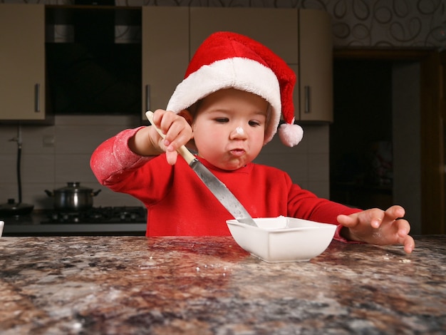 Netter Kleinkindjunge in einer Weihnachtsmütze, die kocht