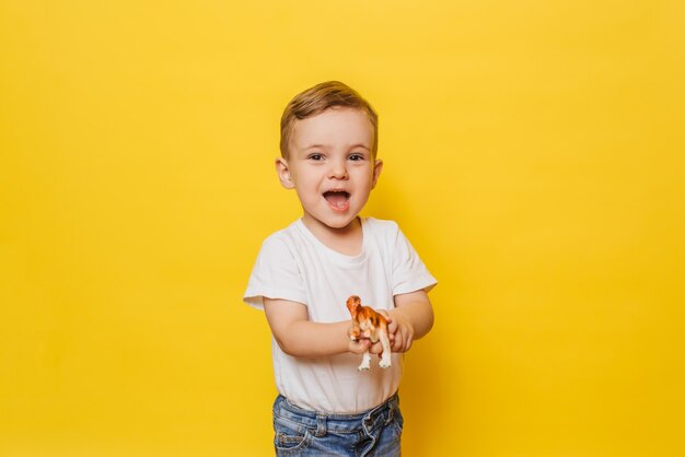 Netter lachender kleiner Junge auf gelbem Hintergrund mit einem Dinosaurierspielzeug in seinen Händen.