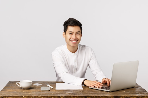 Netter lächelnder asiatischer junger Unternehmer, der im Büro lächelt