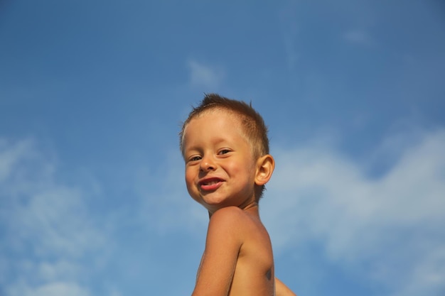 Netter lächelnder kleiner Junge auf Hintergrund des blauen Himmels