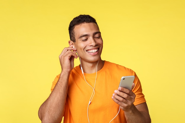 Netter lächelnder männlicher junger Mann im orange T-Shirt, Smartphone halten