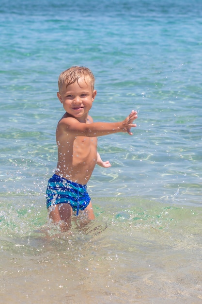 Netter lustiger glücklicher kleiner Junge, der in den Wasserwellen am Seeozean an einem sonnigen Tag spielt