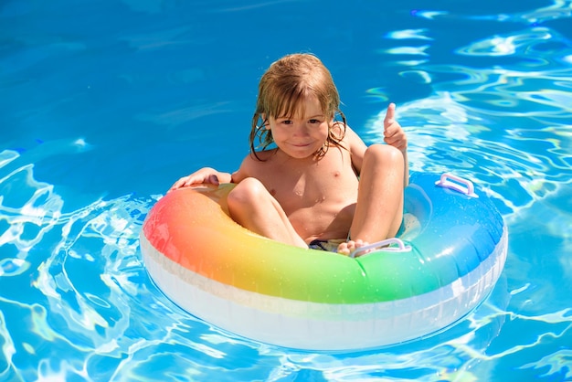 Netter lustiger kleiner Kleinkindkindjunge mit dem Daumen oben in einem bunten Badeanzug und in einer Sonnenbrille relaxin