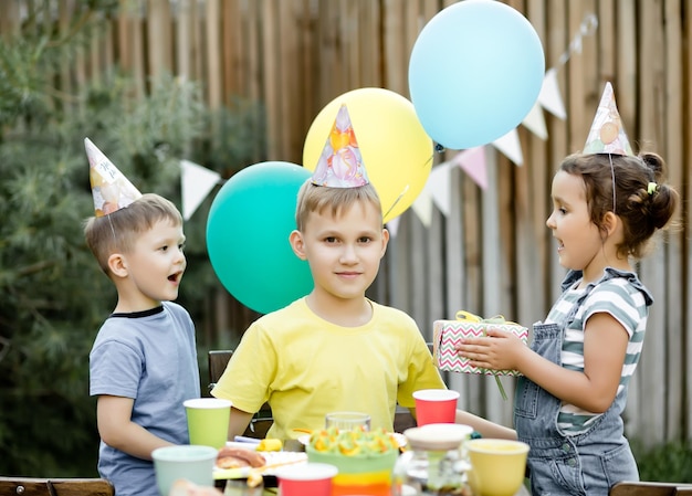 Netter lustiger neunjähriger Junge, der seinen Geburtstag mit Familie oder Freunden mit hausgemachtem gebackenem Kuchen in einem Hinterhof feiert Geburtstagsfeier für Kinder Er bekommt Geschenkbox