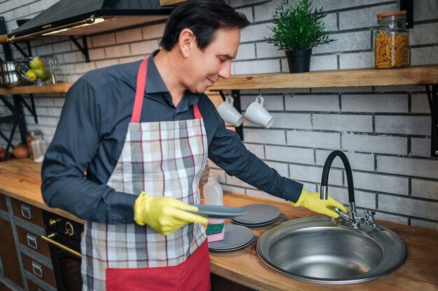 Netter Mann in Apon stehen in der Küche und berühren Waschbecken.