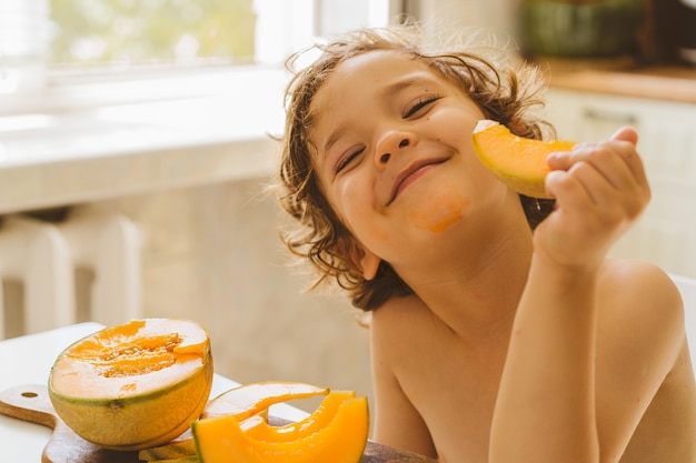 Netter schöner kleiner Junge, der frische Melone isst.