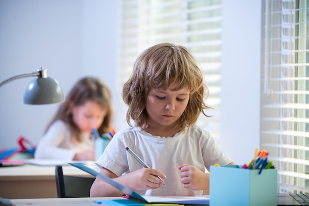 Netter Schüler, der am Schreibtisch im Klassenzimmer des Grundschülerjungen schreibt, der in der Grundschule Test macht