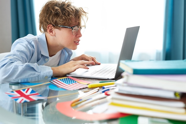 Netter Schüler sagt Hallo vor der Kamera, während er Online-Unterricht zu Hause hat