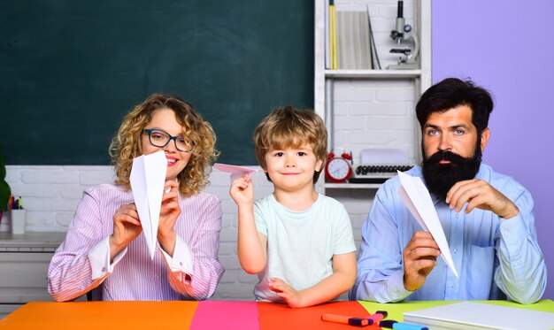 Netter Schüler und seine Eltern, die Papierflieger-Origami-Unterricht machen, Mama und Papa helfen seinem Sohn bei der Bildung