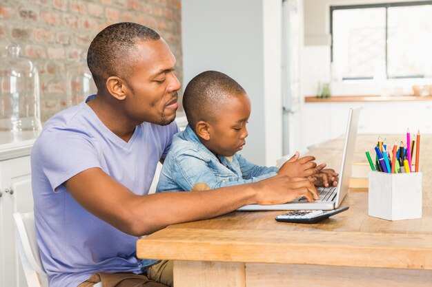 Netter Sohn, der Laptop am Schreibtisch mit Vater verwendet