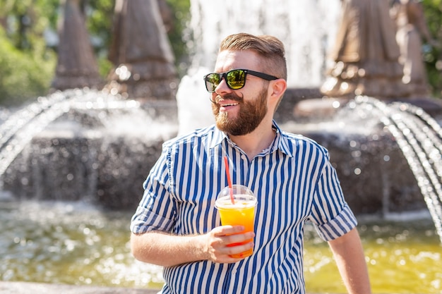 Netter stilvoller junger männlicher Hipster mit einem Schnurrbart und einem Bart und dem Tragen von Gläsern, die Saft mit trinken