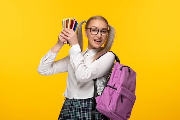 Netter Student des Weltbuchtages in der Uniform, die bunte Bleistifte auf gelbem Hintergrund hält