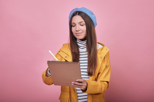 Netter Student mit schönem Lächeln in einer gelben Jacke mit Notizbuch