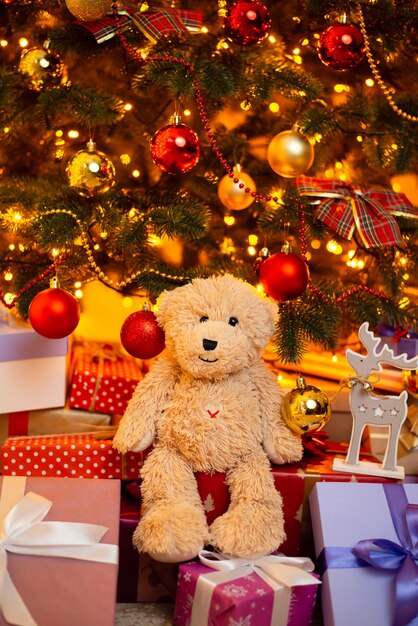 Netter Teddybär, der auf Geschenken unter dem Weihnachtsbaum sitzt