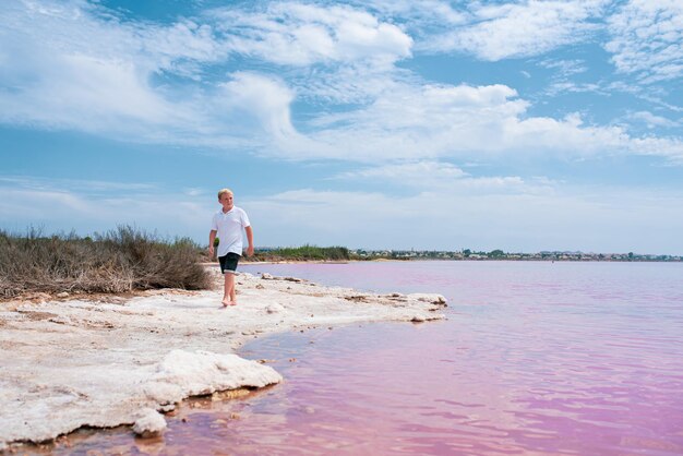 Netter Teenager, der Sommerkleidung trägt und auf dem rosa See spazieren geht