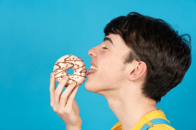 Netter Teenagerjunge, der süßes Schokoladenbrötchen oder Cupcake leckt