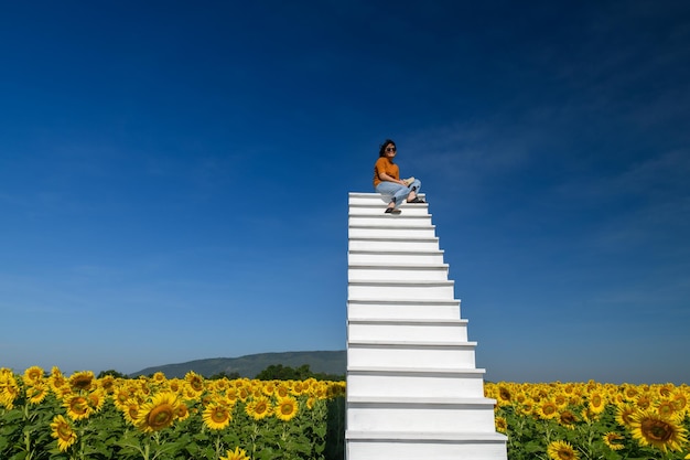 Foto netter tourist, der auf der weißen hohen treppe mit wunderschönem sonnenblumenfeld sitzt