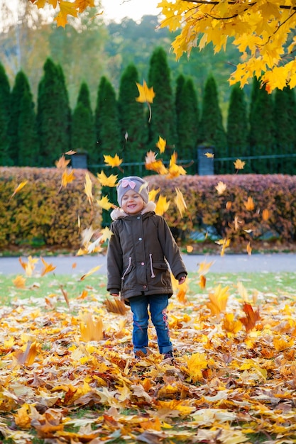 Nettes 3-4 Jahre altes kleines Kindermädchen, das im Herbstpark spielt. Herbstlaub fallen.