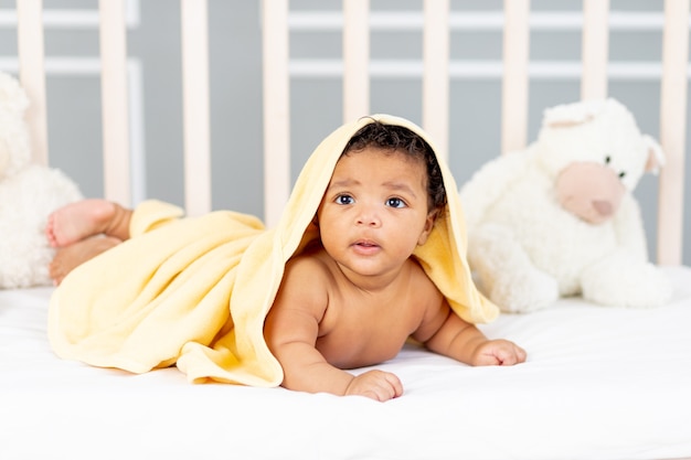 Nettes afroamerikanisches kleines Baby, das nach einem Bad in einem gelben Handtuch im Bett liegt