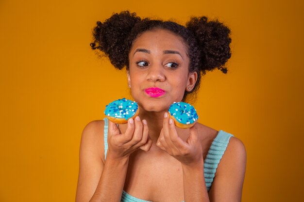Nettes Afromädchen, das zwei bunte Donuts hält. Afrofrau mit Donuts