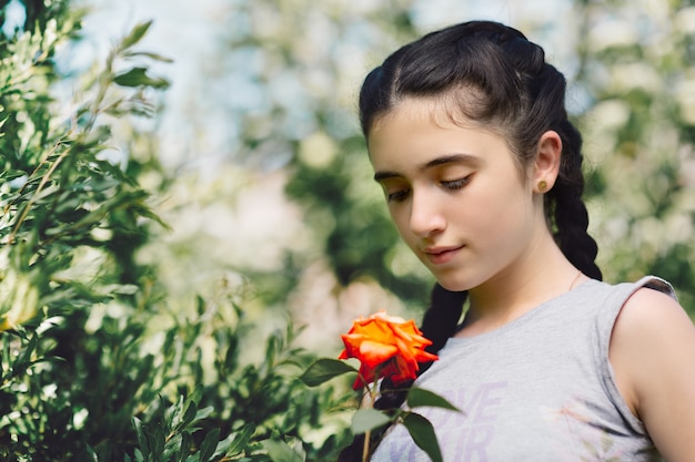 Nettes armenisches Mädchen, das Rose im Garten hält und betrachtet